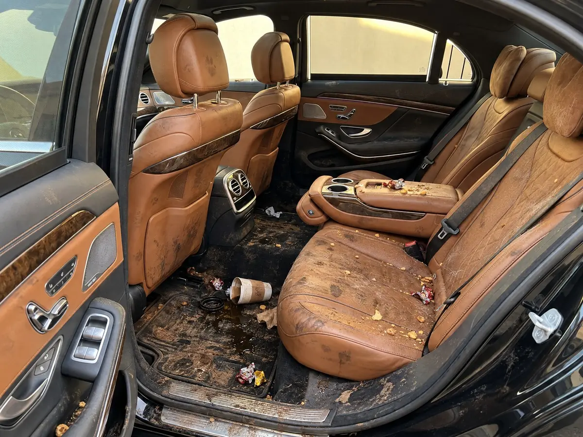 Car backseat before detailing, covered in crumbs, pet hair and a spilled coffee